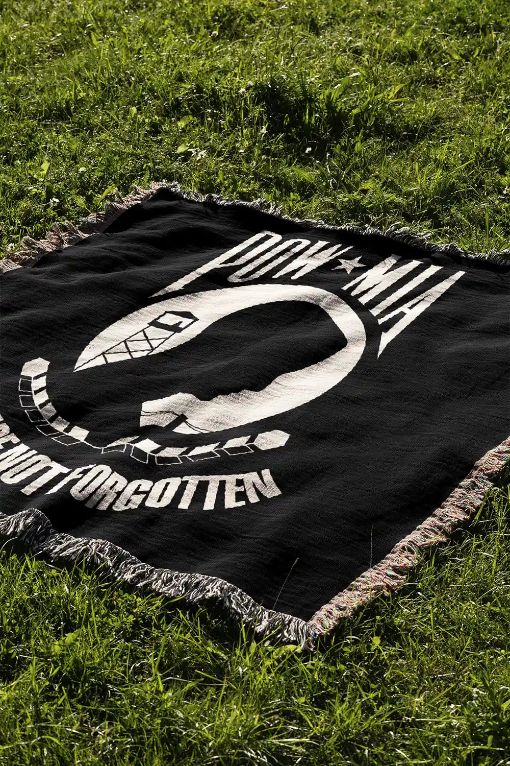 Black and white tapestry of POW MIA flag laying in a grass field