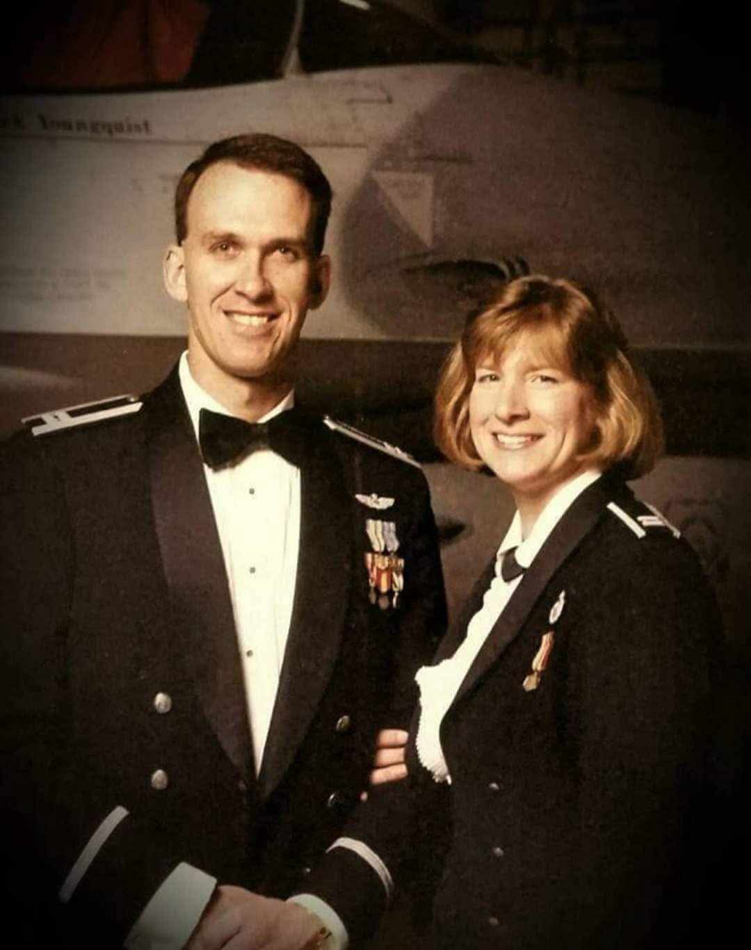 Man and women posing in black Air Service service dress uniforms in front f an aircraft