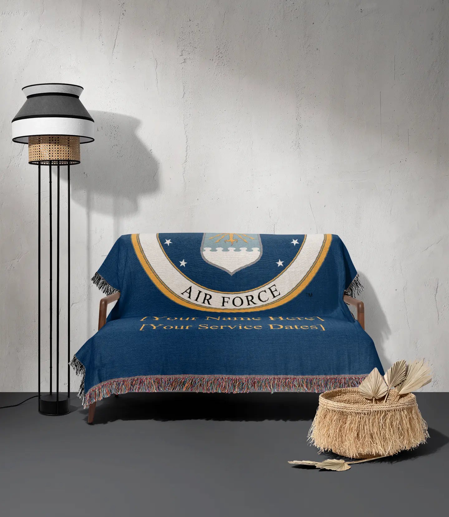 Air Force emblem with solid gold text for customer name and service dates on a blue background draped on a small love seat next to a straw basket and a floor lamp.